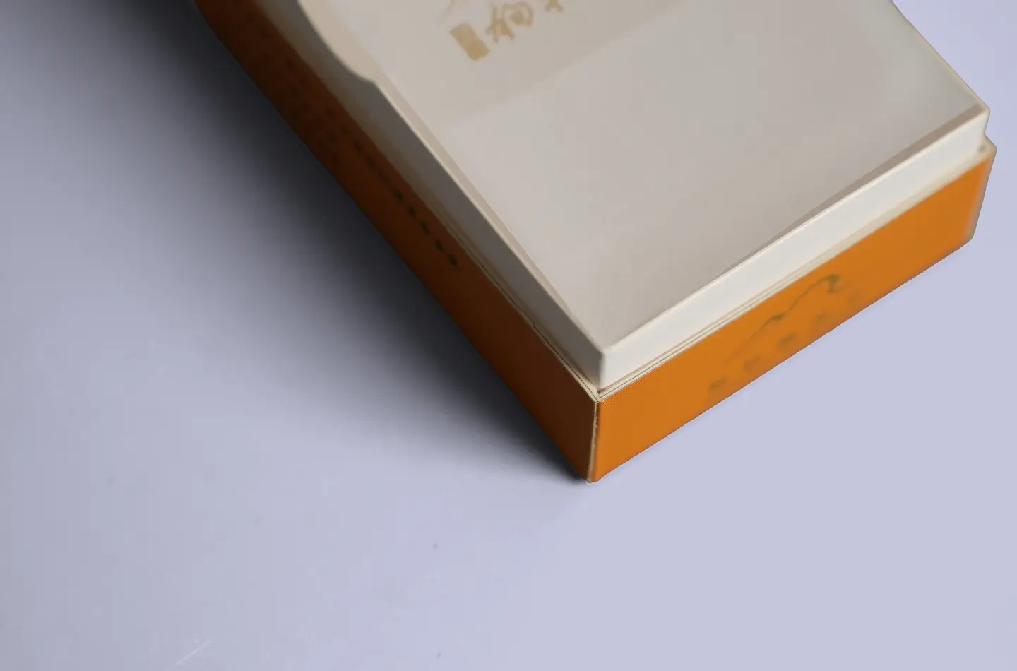 Custom orange-yellow coated flip-top paperboard box, close-up of edge and gold foil accents
