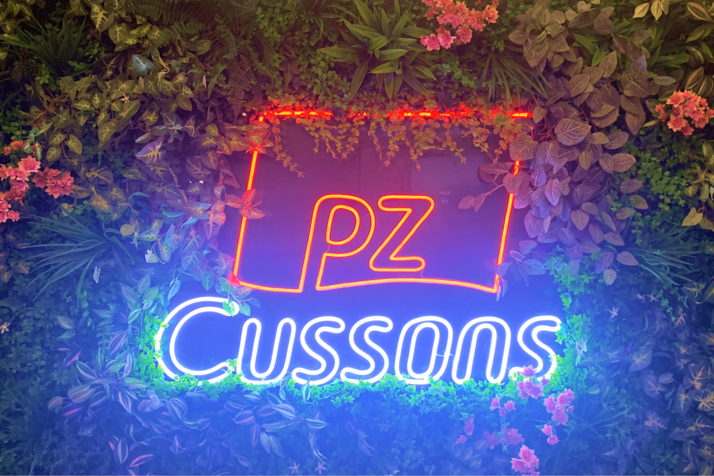 Neon PZ Cussons sign surrounded by plants and flowers