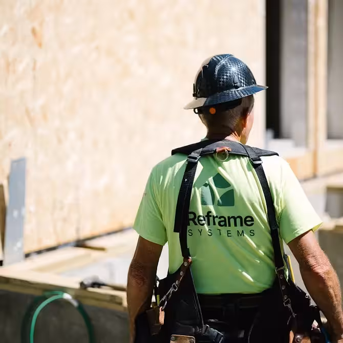 Construction worker wearing a Reframe Systems shirt and hard hat, walking at a job site.