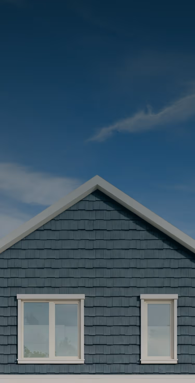 Blue siding on house with two white-framed windows under a clear blue sky with clouds.