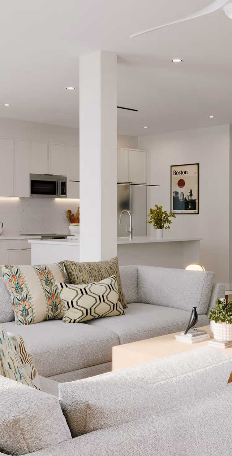 Modern living room with light gray sofas, patterned pillows, coffee table, and open white kitchen in background.