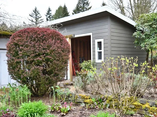 Backyard building with gray horizontal siding beside a planted garden