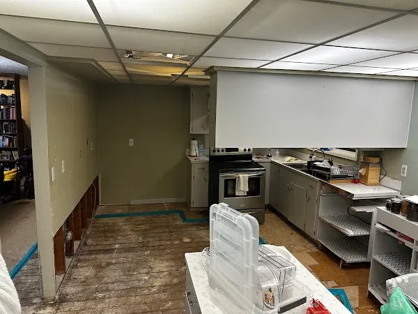 Kitchen renovation with exposed subfloor and an unfinished wall beside white cabinets