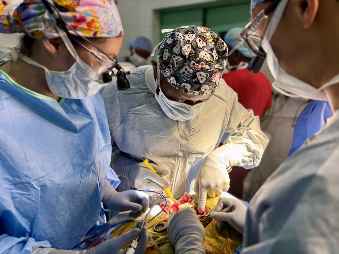 From left to right: Dr. Silvia Vaca, neurosurgeon Dr. Alieu Kamara, and Dr. Seunggu Han operate on Morie Abibu's to remove a mass is growing at the base of his skull, pressing against his spinal cord and paralyzing him from the neck down.Sophia Li for NPR