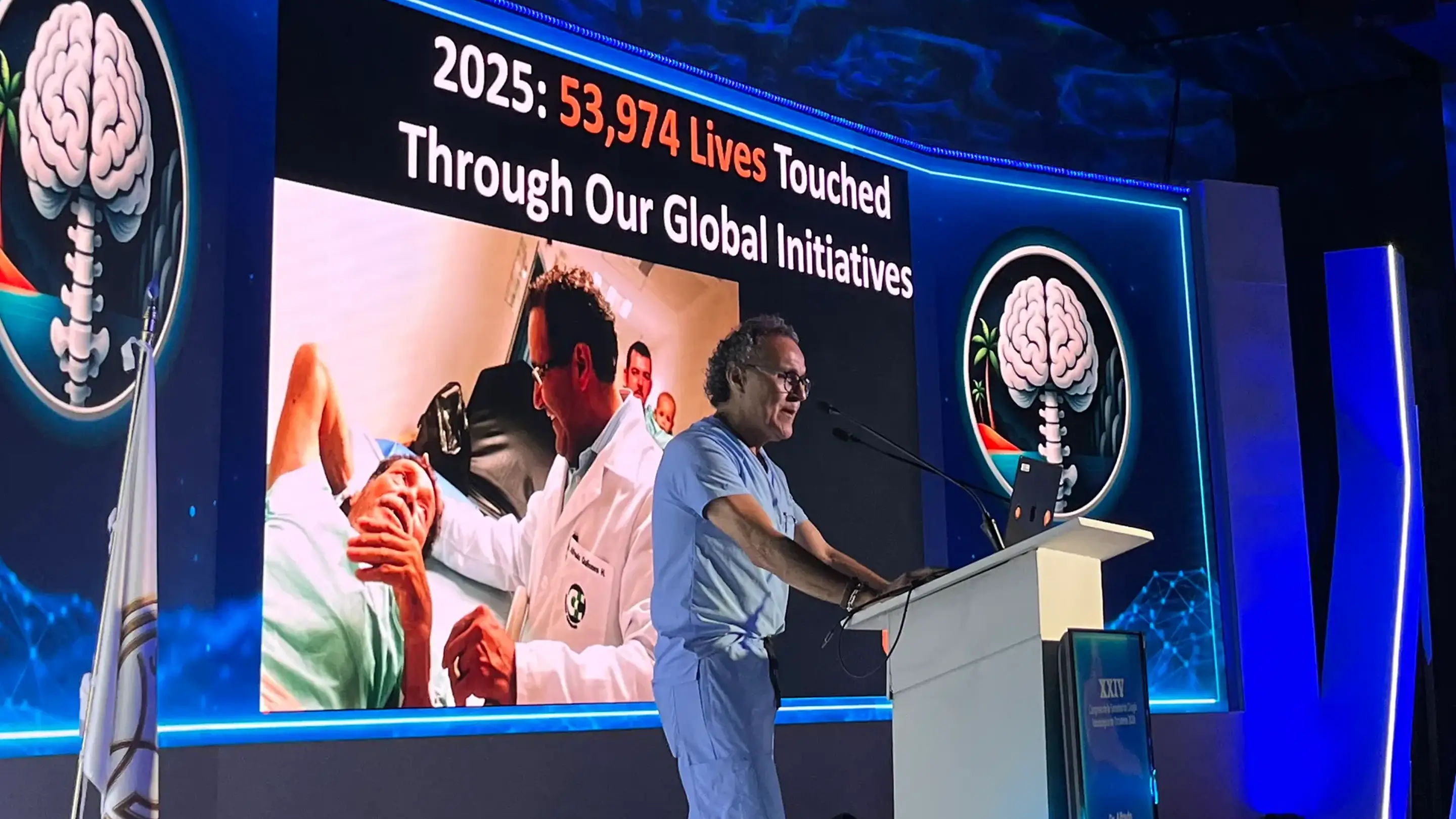 Dr. Alfredo Quiñones-Hinojosa presents at a podium during the SCNO Congress, in front of a large screen displaying '2025: 53,974 Lives Touched Through Our Global Initiatives' above a photo of a physician with a patient.