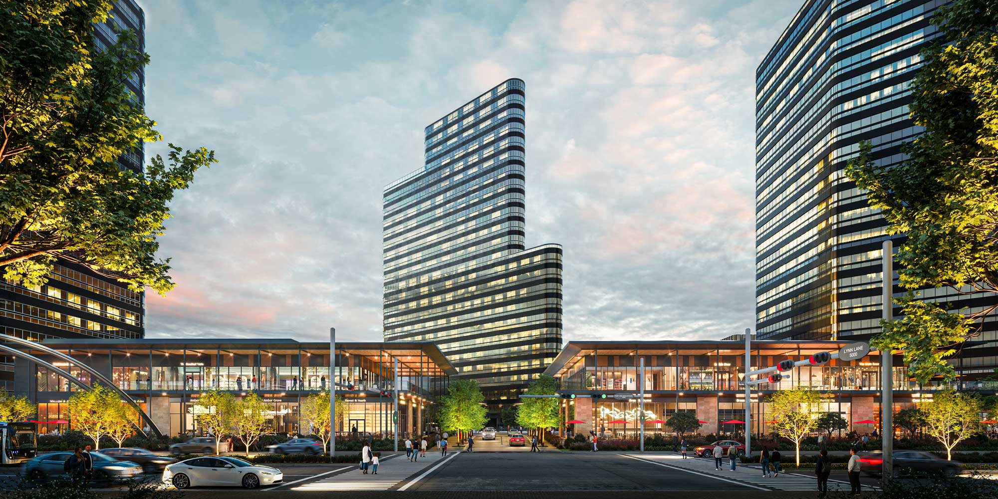 Modern glass buildings with shops and trees lining a busy urban street at dusk.