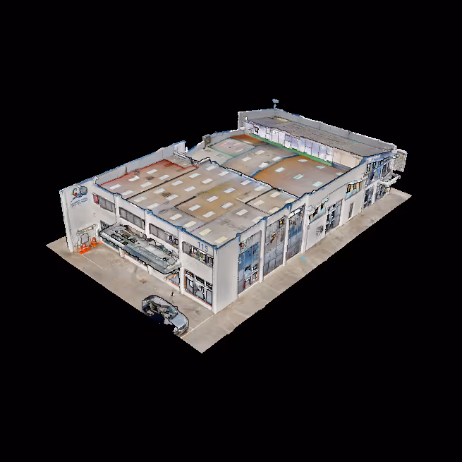 Aerial view of a large industrial warehouse building with multiple garage doors and a car parked outside on concrete pavement.