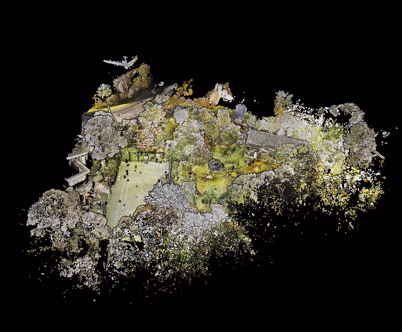 Aerial view of a green garden with trees, a small building, pathways, and a grassy lawn surrounded by dense foliage.