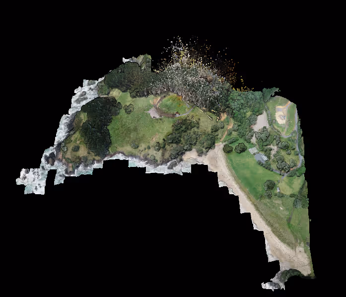 Aerial view of a coastal park featuring grassy areas, dense trees, rocky shoreline, and pathways.