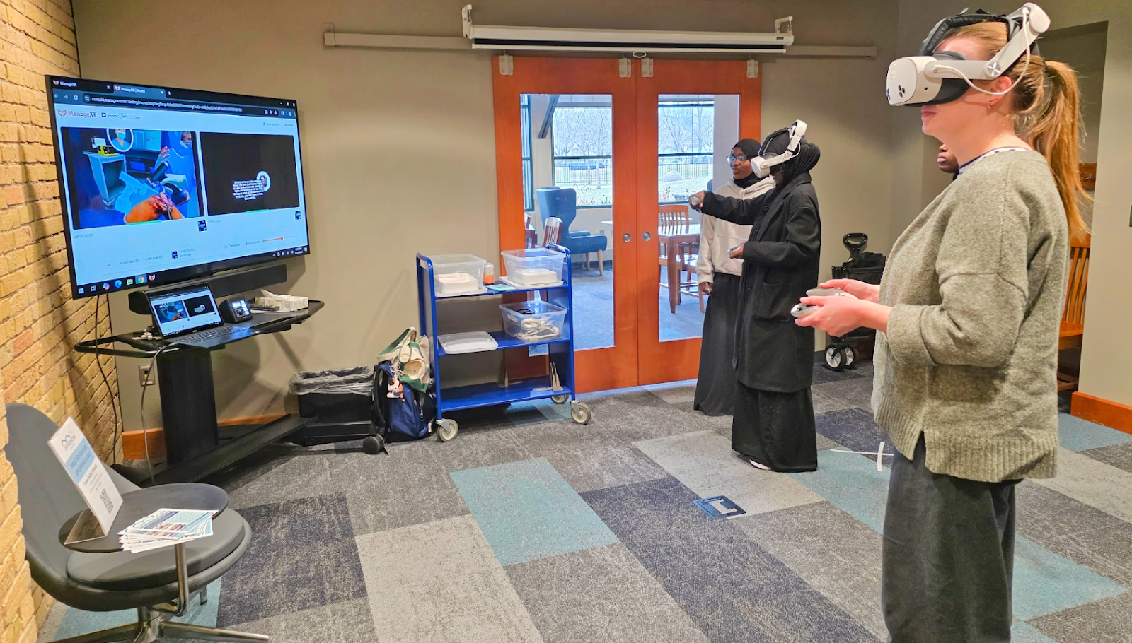 Two women wear a VR headset and experience a career simulation. 