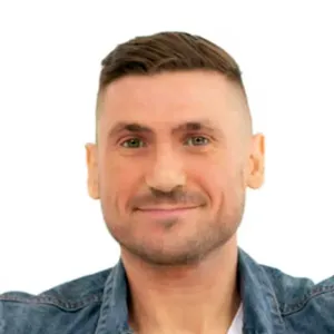 Man with short brown hair and a light beard smiling, wearing a blue denim shirt.