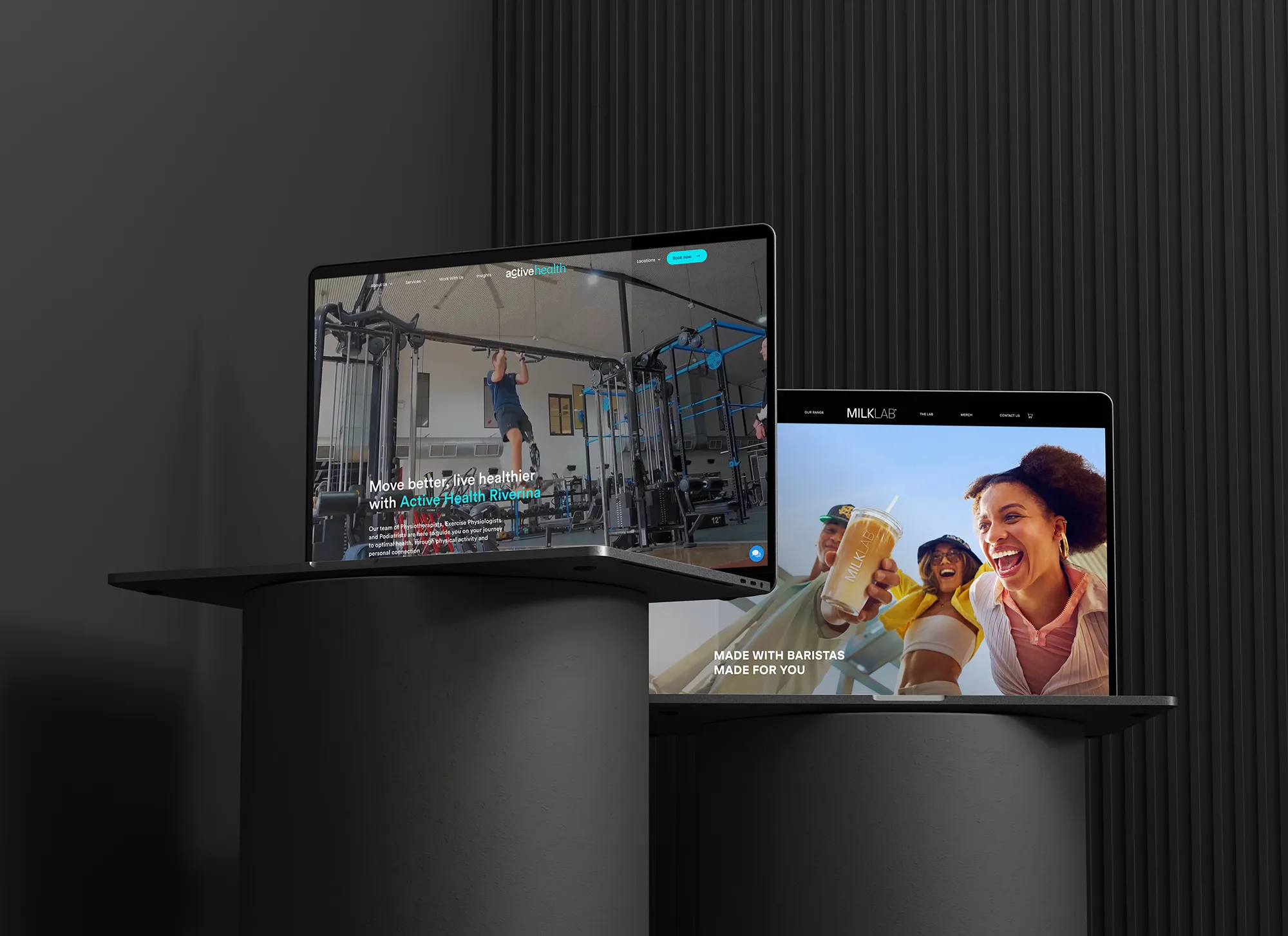 Two laptops on cylindrical pedestals displaying websites: one shows a gym scene with a person doing pull-ups, the other shows smiling people holding a branded drink.