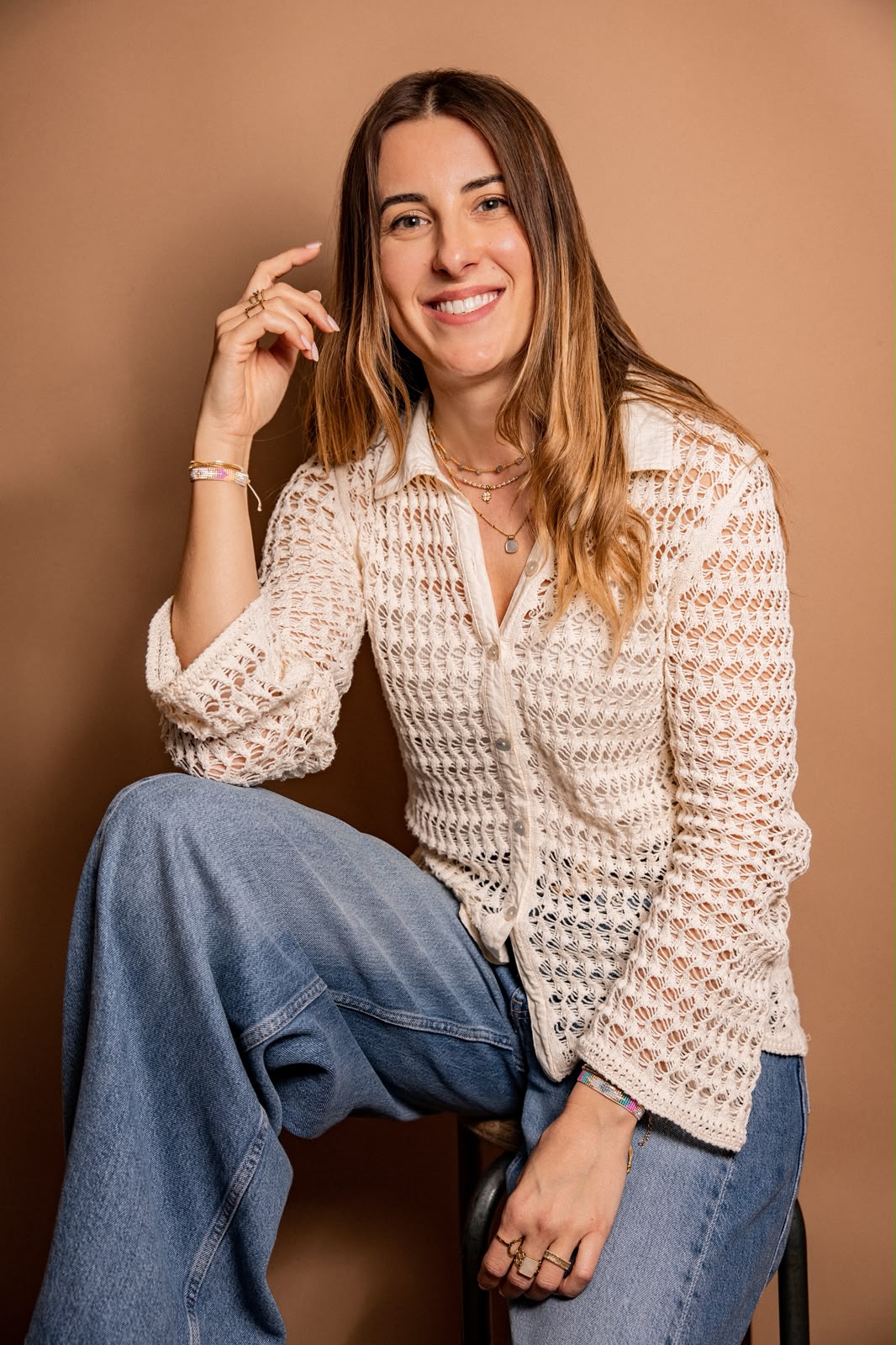 Femme souriante assise, portant un haut en crochet blanc et un jean bleu clair.