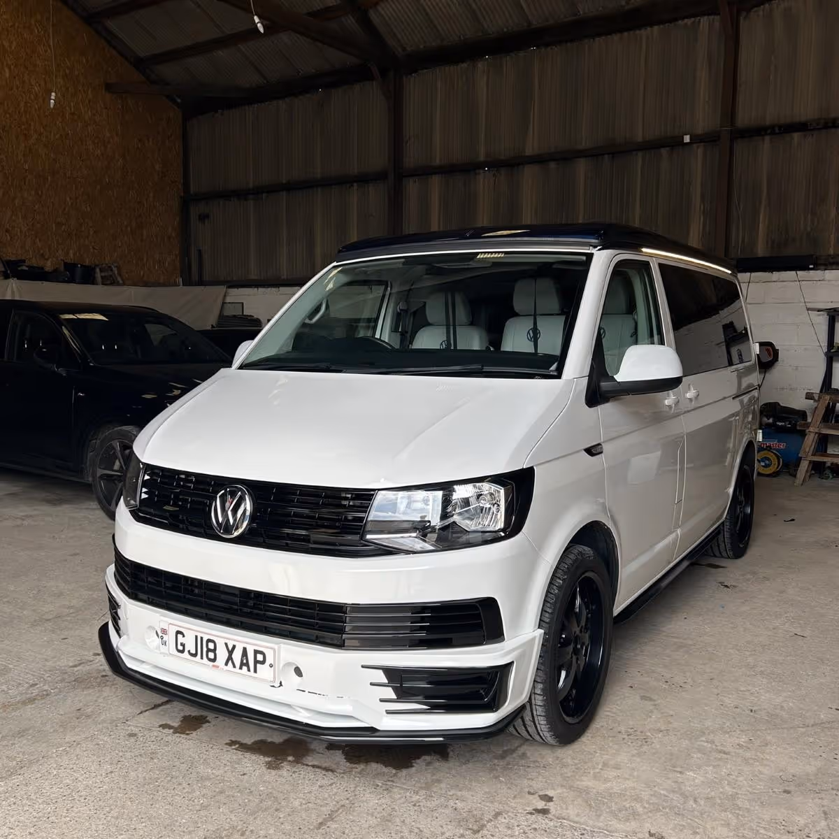 White Volkswagen van with black roof and black wheels parked inside a garage.