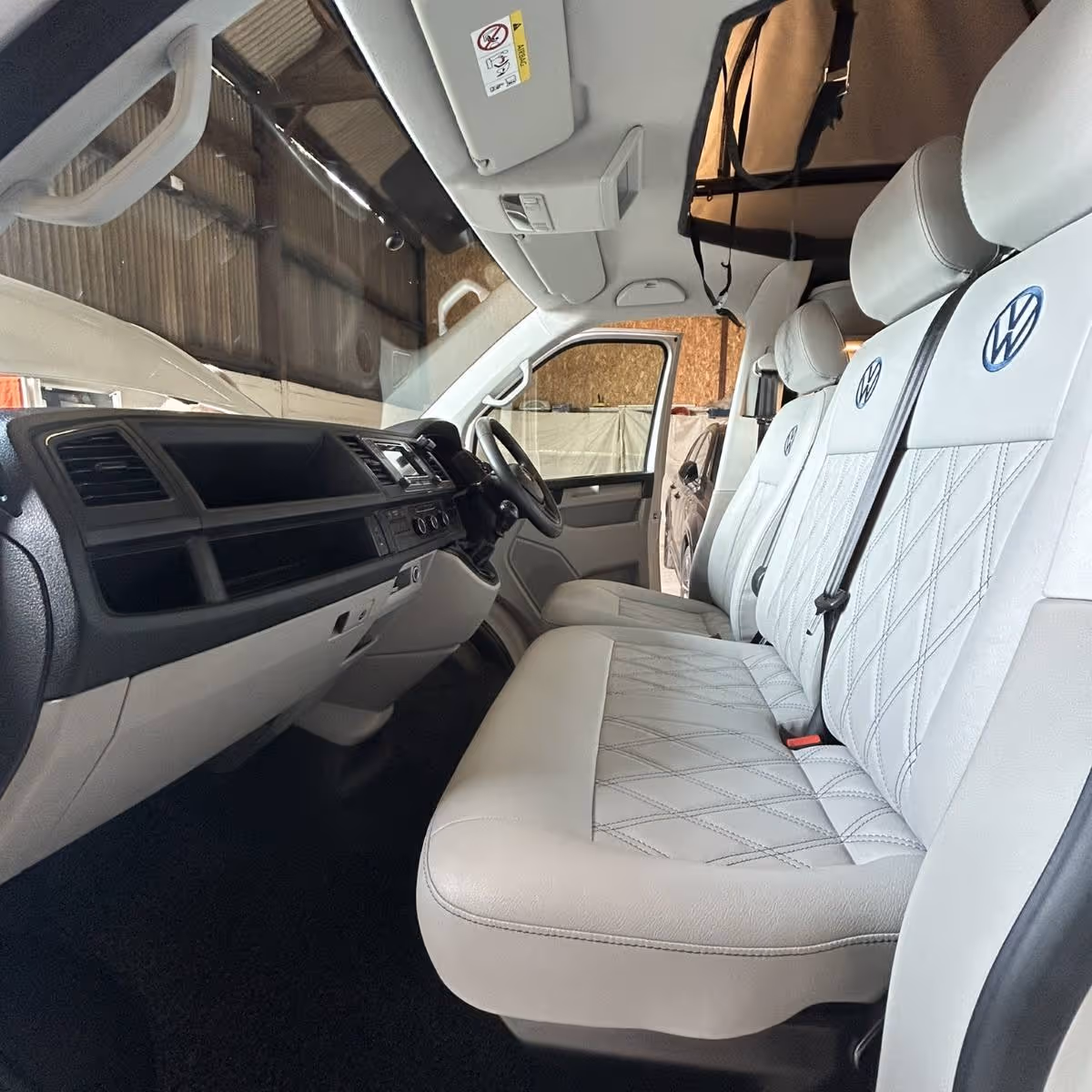 Interior of a Volkswagen vehicle showing the front passenger seats upholstered in white leather with diamond stitching and VW logos on the headrests.