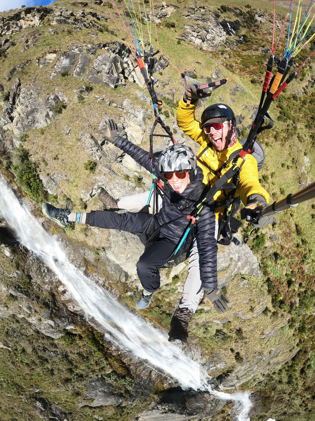 Paraglider soaring above stunning Lake Wānaka with snow-capped mountains and a clear blue sky in the background, showcasing a breathtaking aerial view of the scenic landscape.