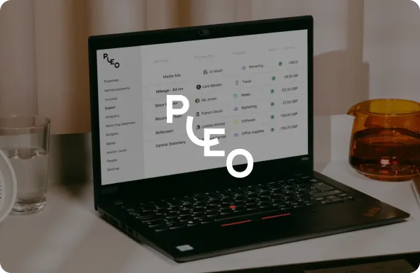 Black laptop on a white desk displaying expense management software with a glass of water and an amber transparent glass next to it.