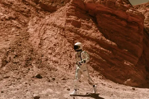 Person wearing a silver astronaut suit and white helmet walking on rocky, reddish terrain.