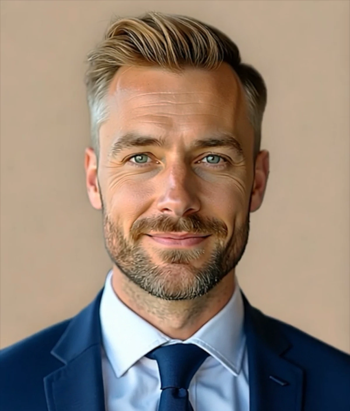 Smiling man with light brown hair and beard wearing a blue suit, white shirt, and blue tie against beige background.