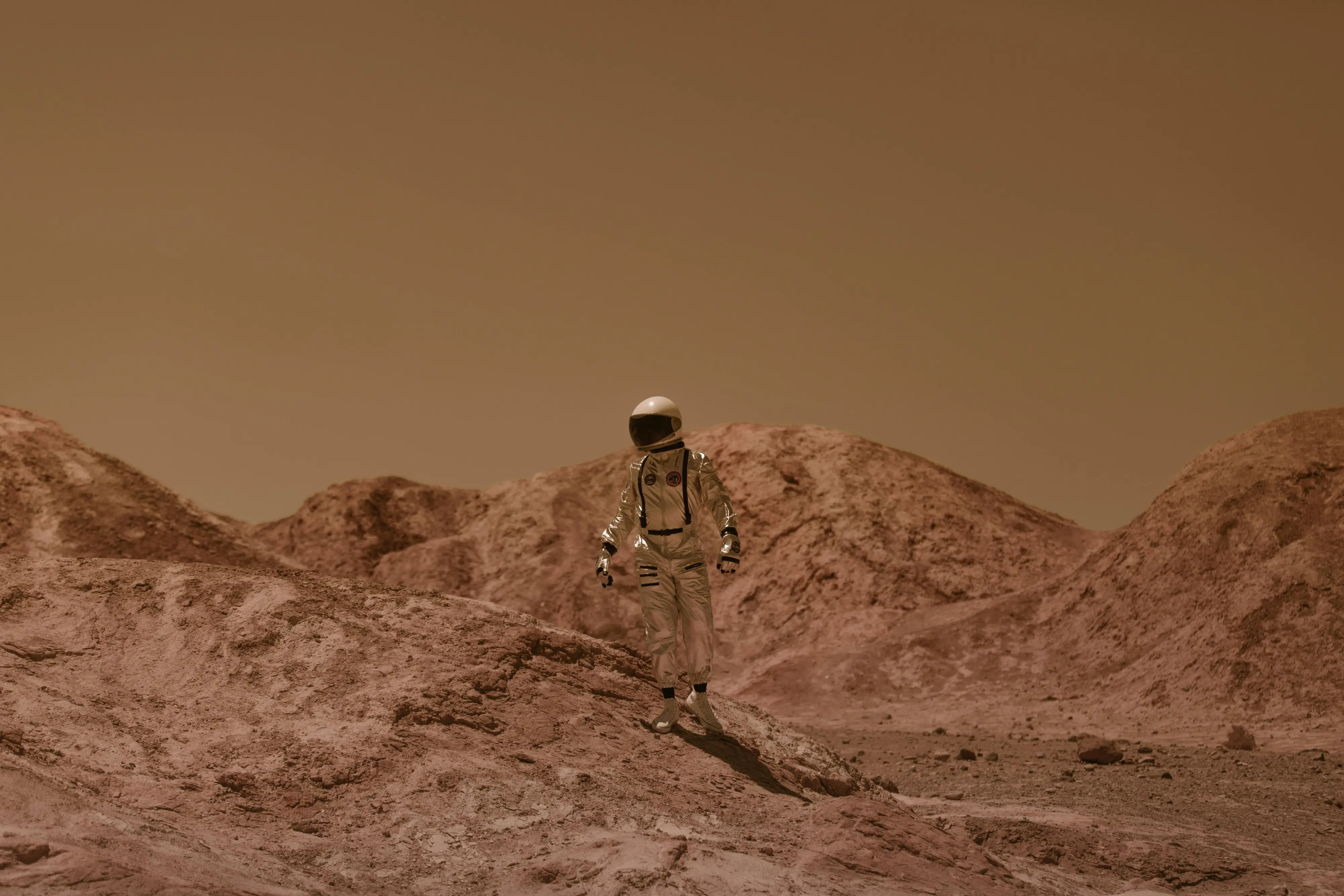 Astronaut in a white spacesuit standing on rocky, reddish terrain resembling Mars.