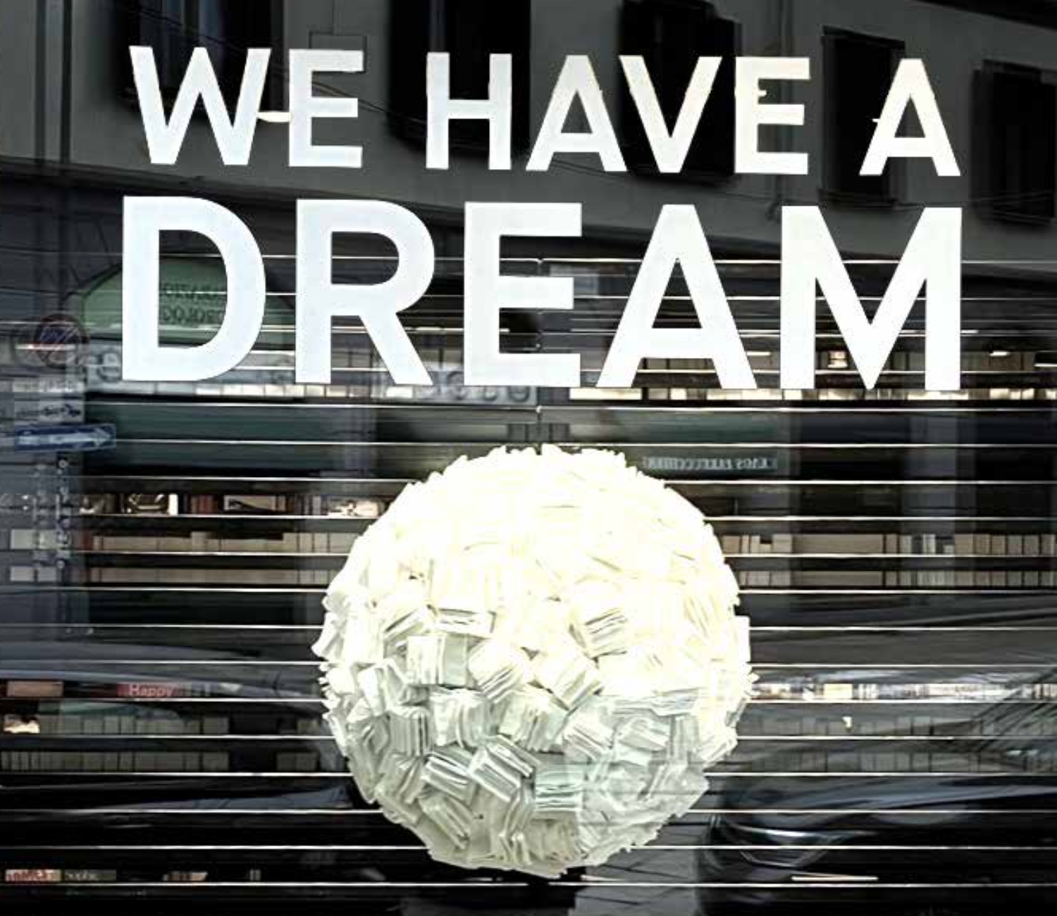 Scritta 'WE HAVE A DREAM' sopra una sfera tridimensionale fatta di messaggi bianchi su uno sfondo urbano riflettente.