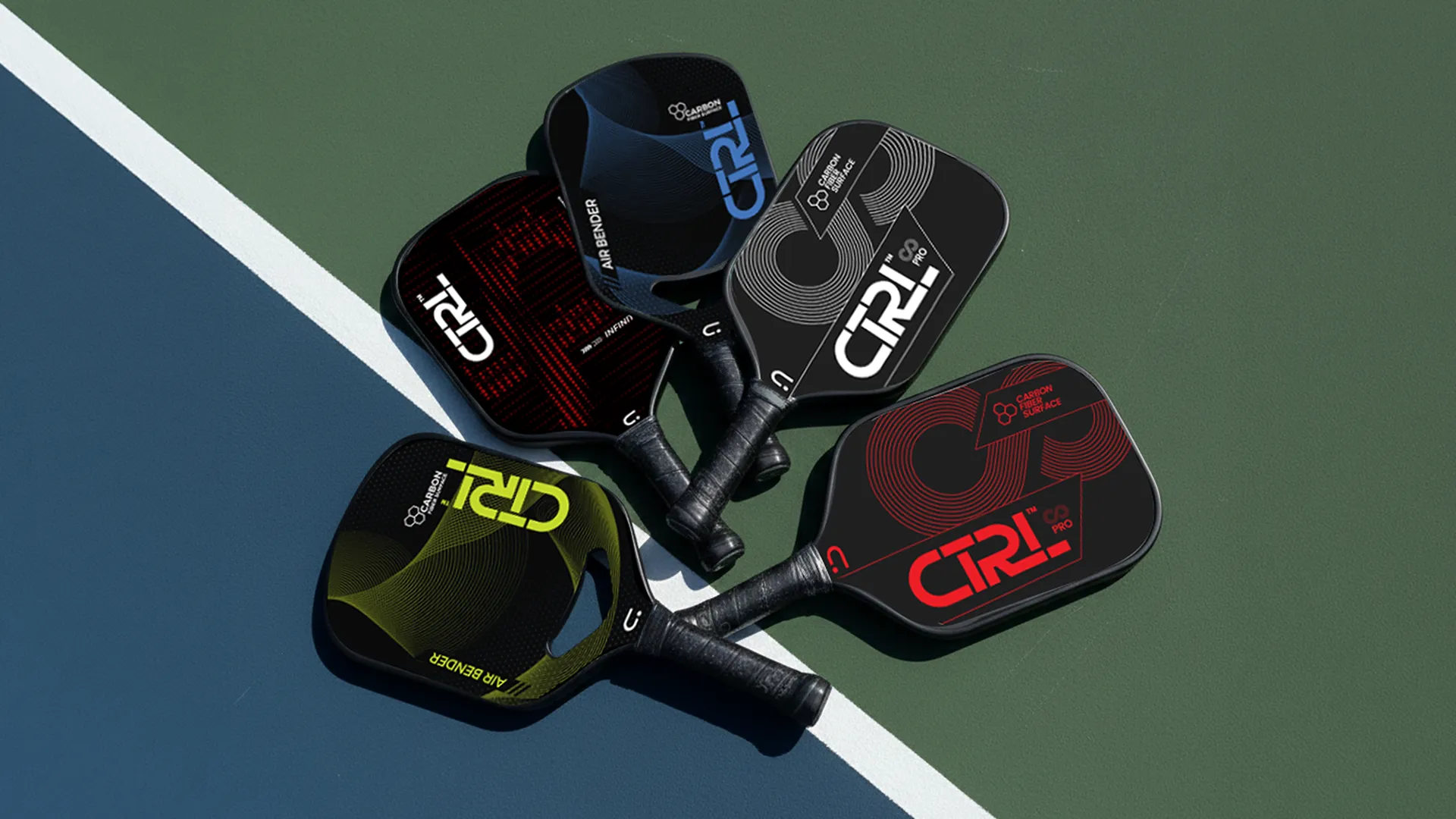 Five pickleball paddles with colorful modern designs and the brand name CTRL arranged in a fan shape on a pickleball court near the boundary line.