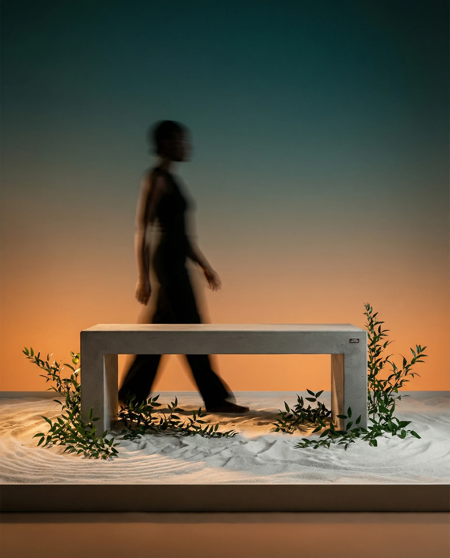 MONO in einer inszenierten Sandlandschaft mit Zweigen, warmem Licht und einer vorbeigehenden Person.