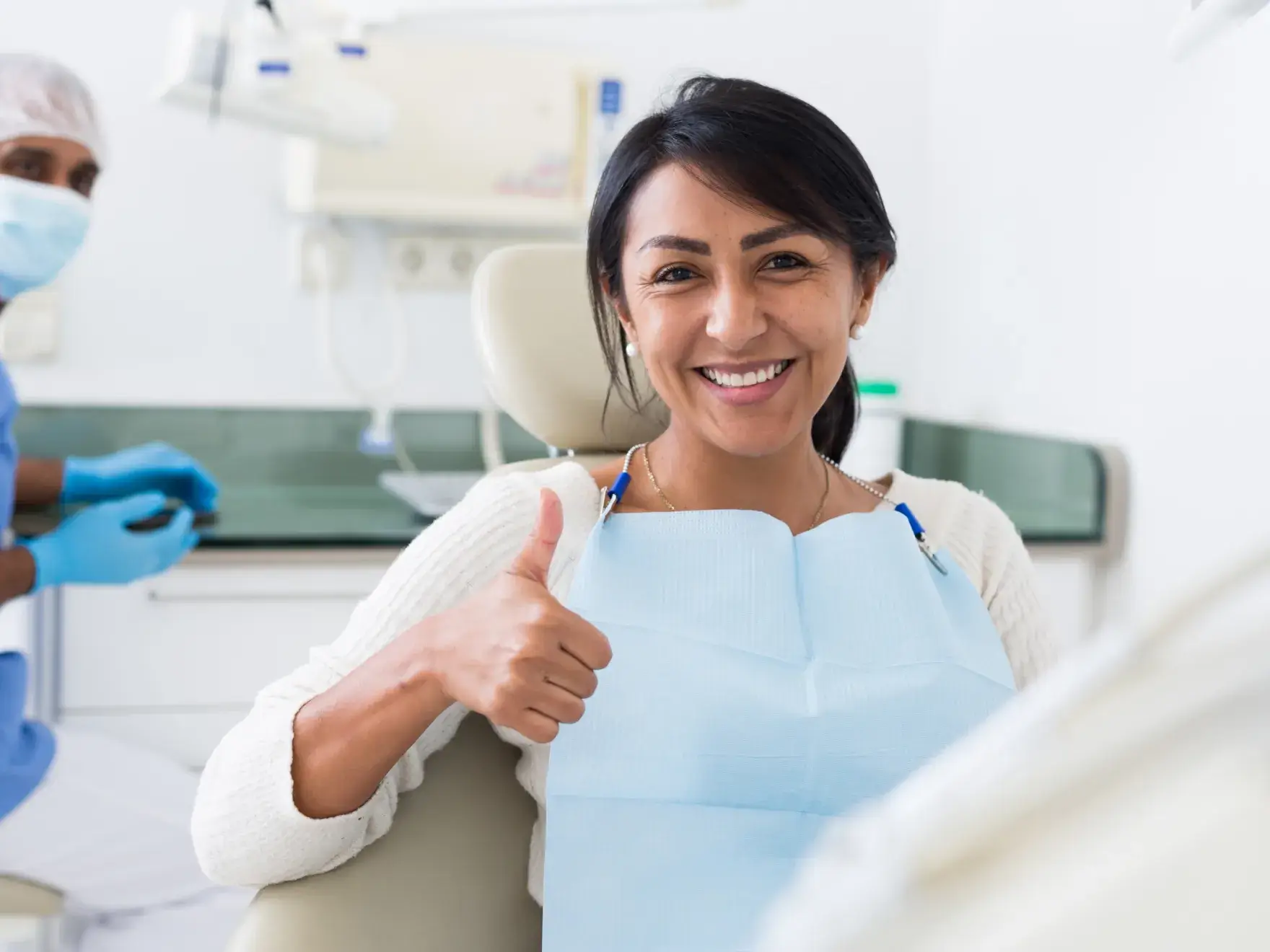 A woman in a dentist chair giving a thumbs up.