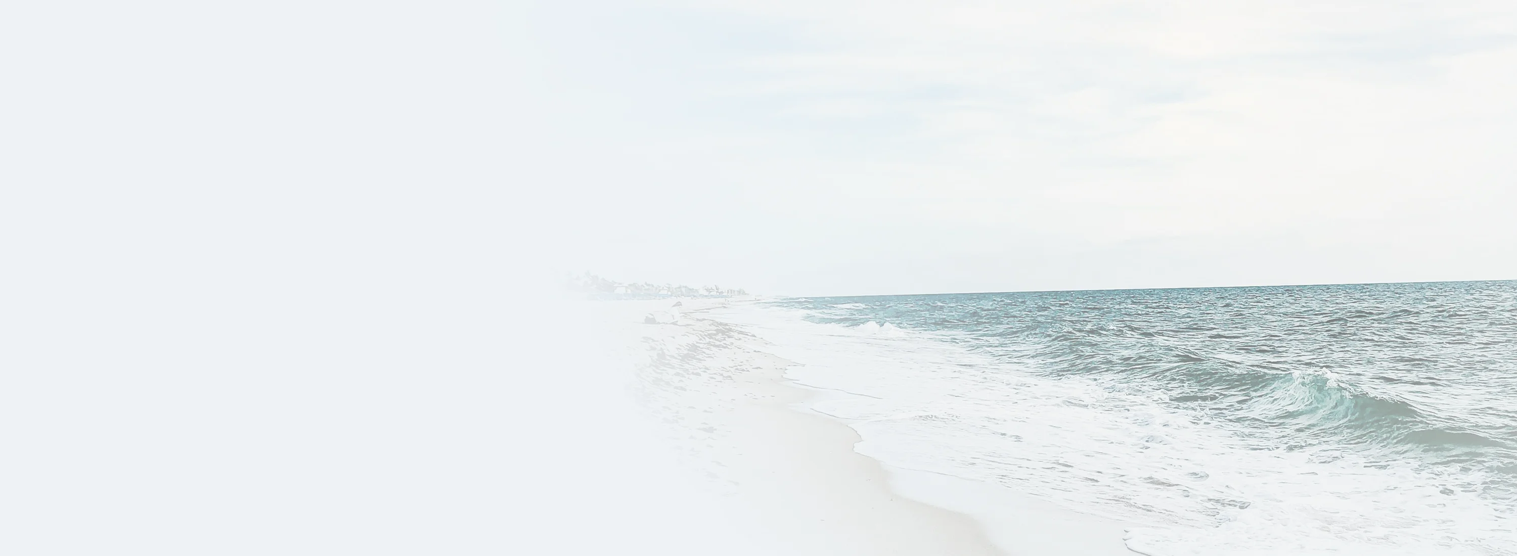 A calm beach landscape showcasing ocean waves beneath a pale white sky.