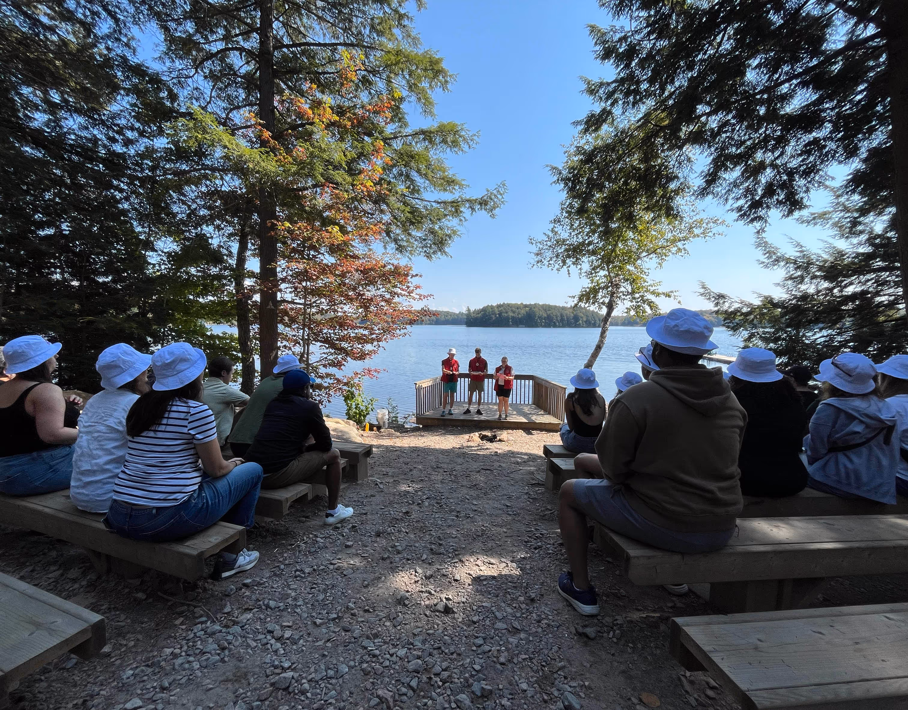 A group of people sitting outside, looking at three people standing.