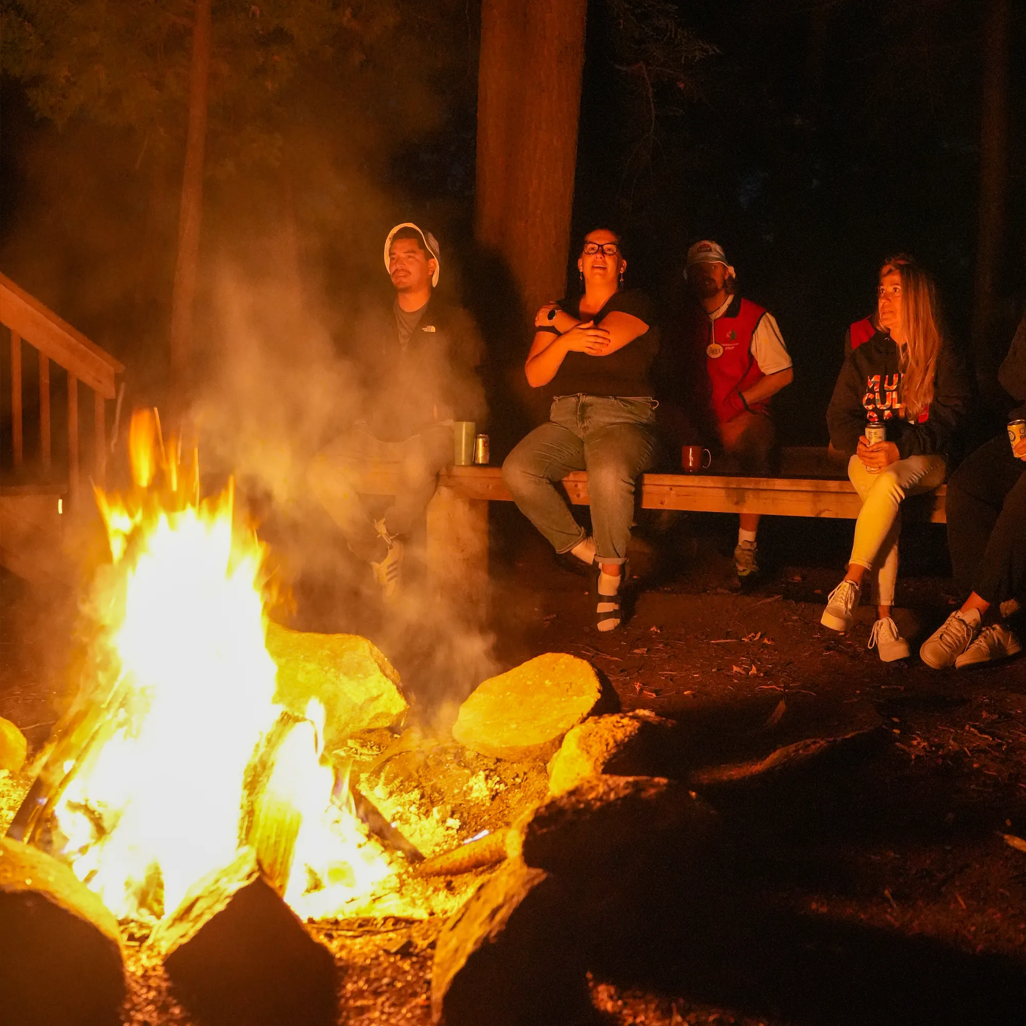 People sitting on a bench by a bonfire.