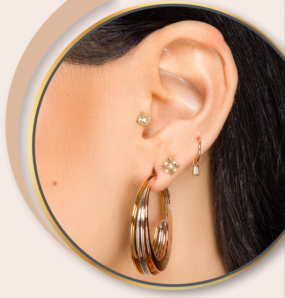 Nahaufnahme eines Ohrs mit mehreren goldenen Ohrringen, darunter ein großer dreifacher Creolenring und kleine Ohrstecker.