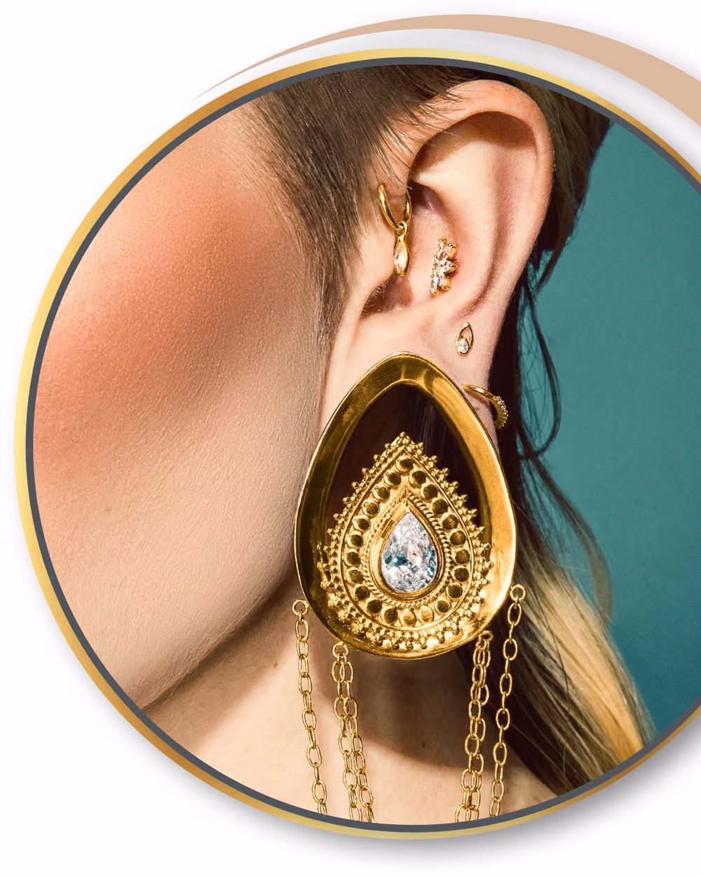 Nahaufnahme eines Ohrs mit mehreren goldenen Ohrringen, darunter ein großer goldener Tropfenohrring mit Ketten.