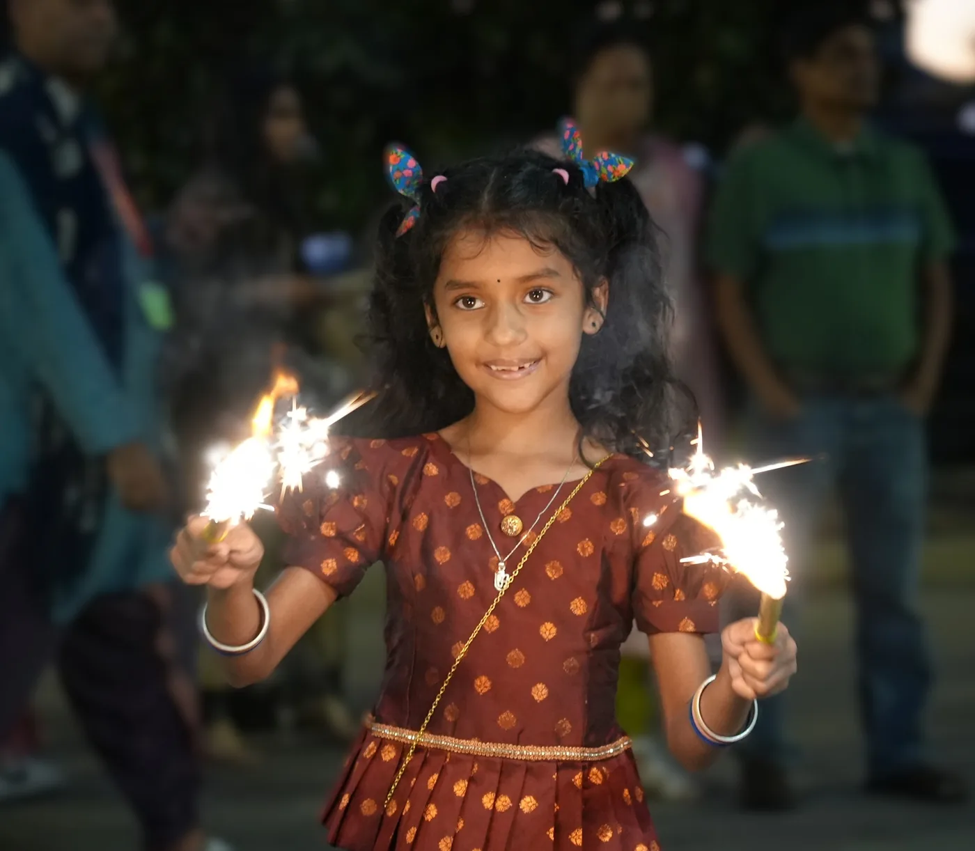 A smiling girl holding lit sparklers at the temple Diwali celebration