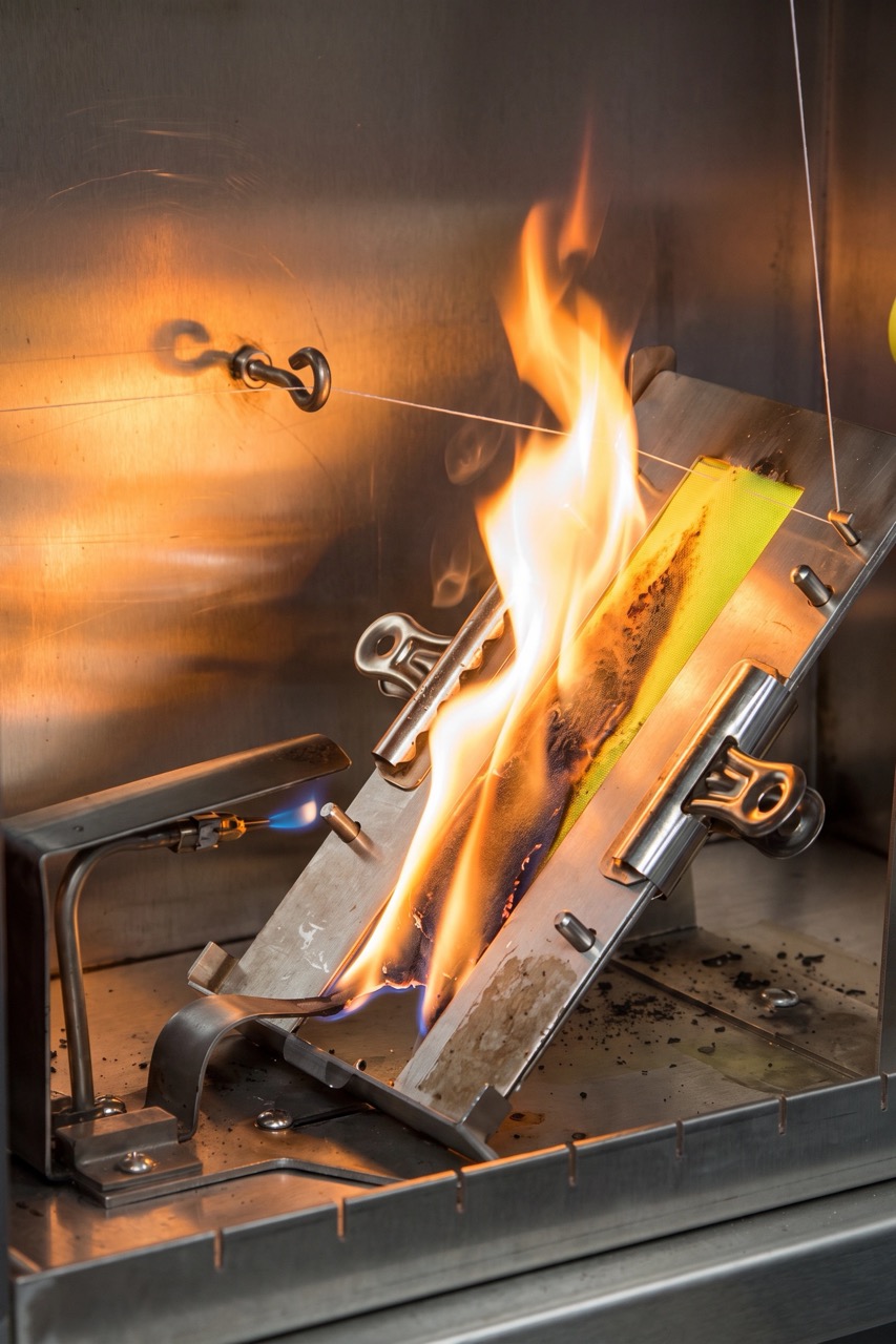 Fabric flame test: a sample clamped at an angle in a test rig with a burner applying flame at the base