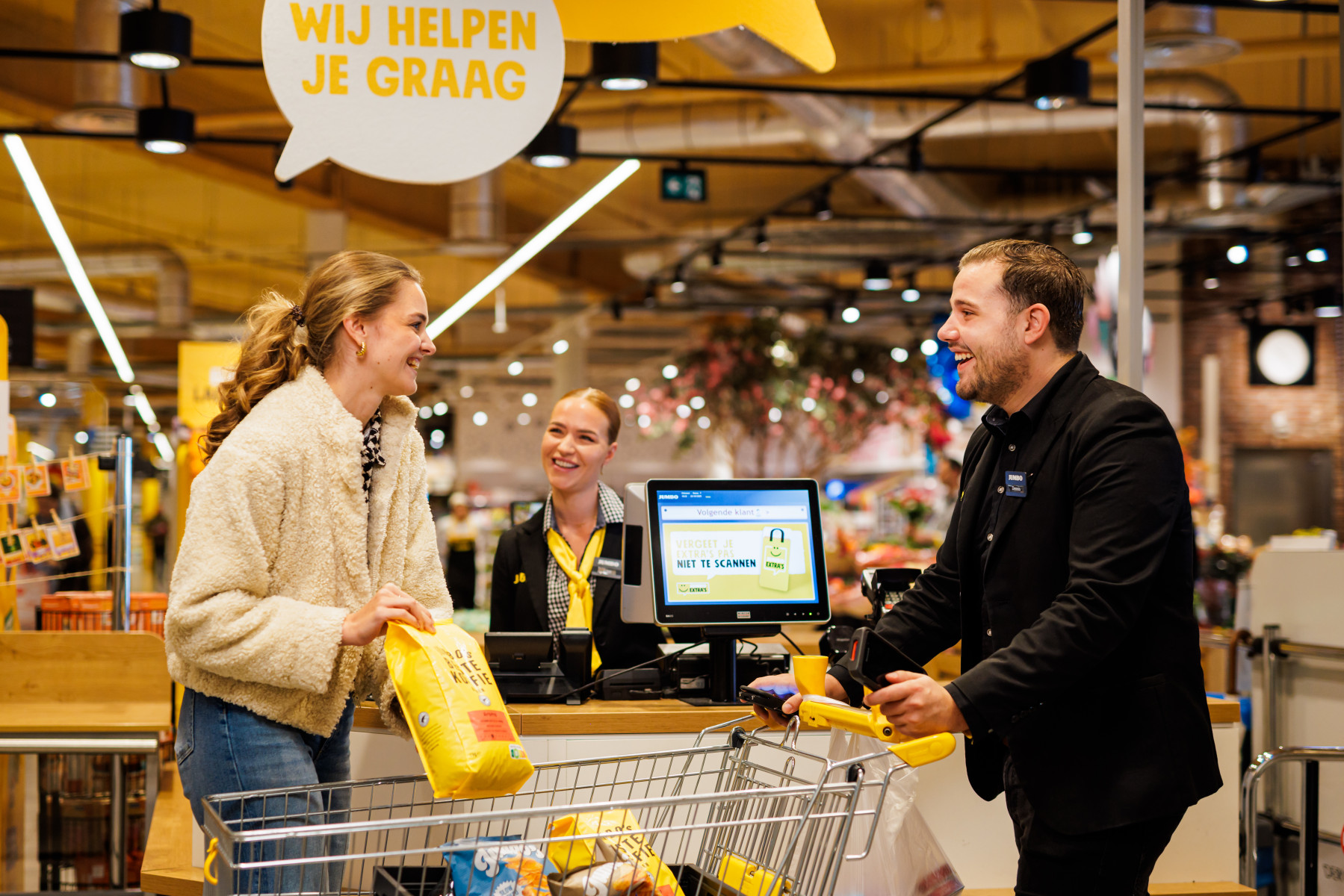 Ein Jumbo-Mitarbeiter hilft einer Kundin an der Self-Scan-Kasse in einer Jumbo-Filiale