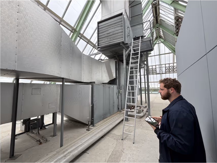 Een man controleert een groot ventilatiesysteem in een industrieel gebouw, mogelijk gerelateerd aan energiebesparing of verduurzaming.