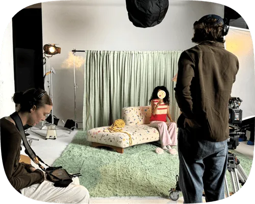 Behind-the-scenes photo shoot with a woman sitting on a bed while crew members work with lighting and camera equipment