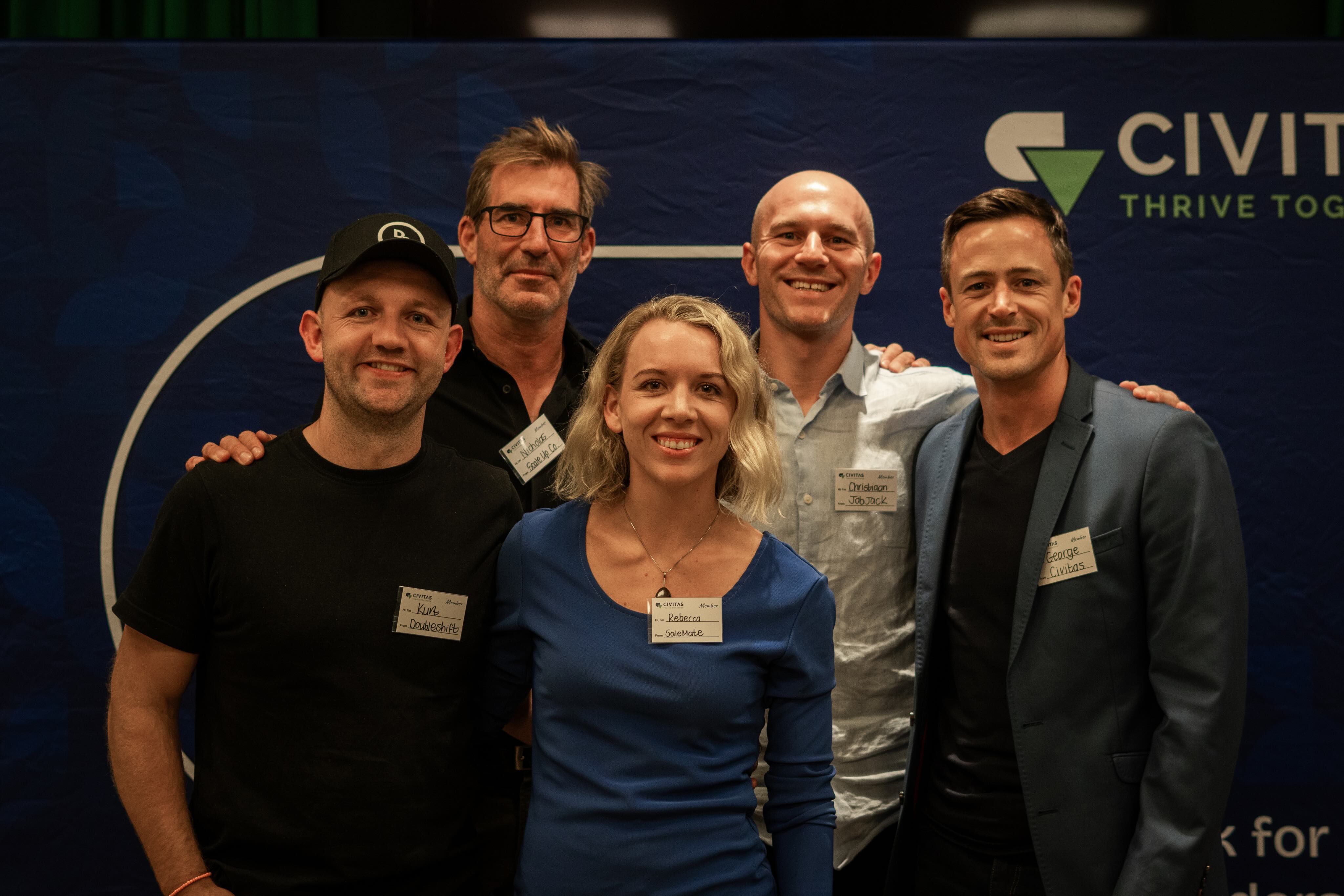 Group of five smiling adults posing together at a Civitas event with name tags visible.