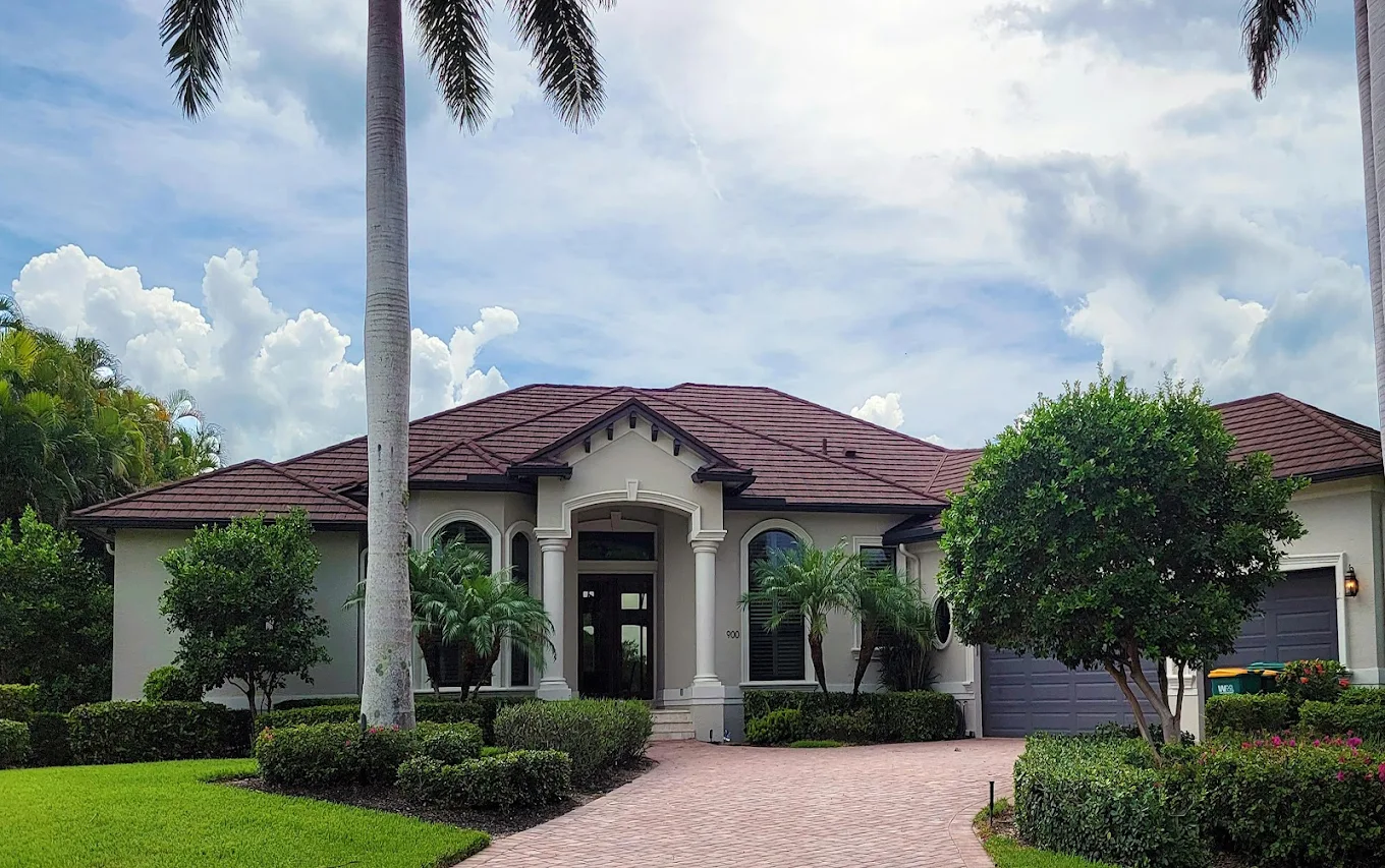 Single-story house with red roof, arched entrance, palm trees, and manicured green lawn.