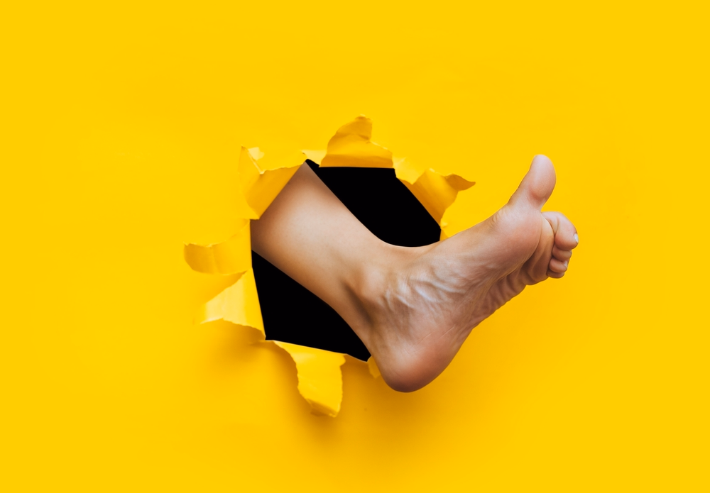Foot breaking through a yellow paper wall as a symbol for podiatry