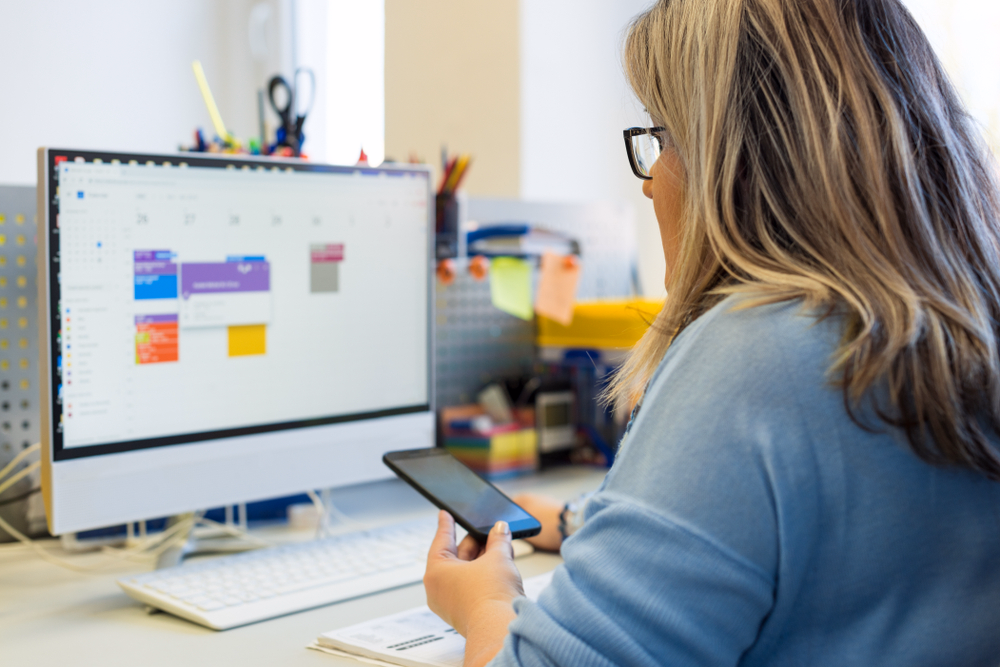 Assistente di studio gestisce gli appuntamenti al computer tenendo uno smartphone