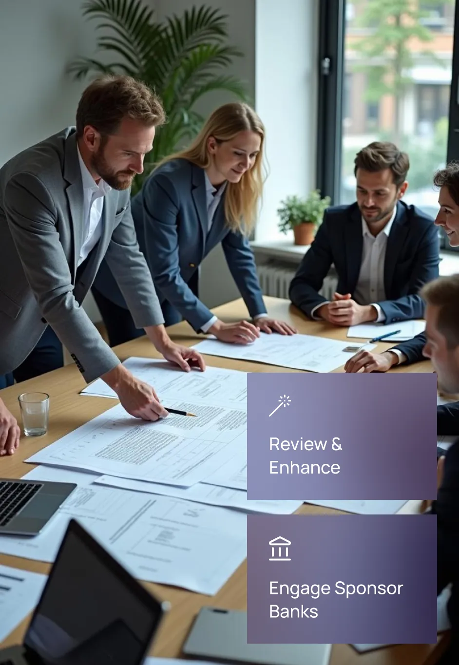 A team collaborating around a table with documents, illustrating Fraxtional's review and enhancement of policies and procedures to engage sponsor banks.