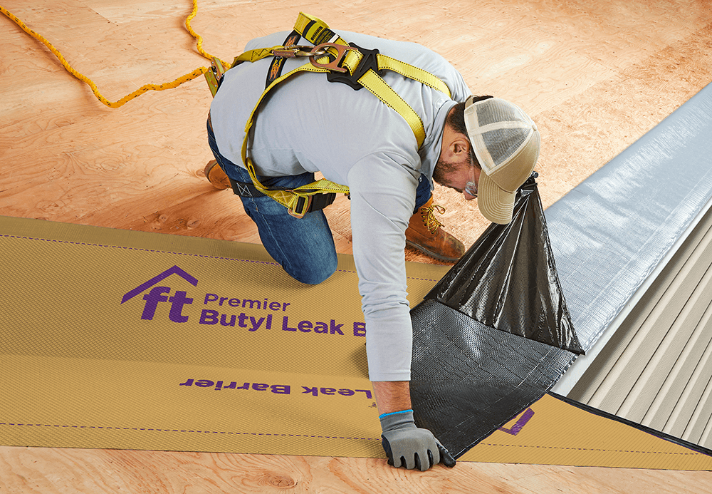 Close-up of the installation process of Premier Butyl Leak Barrier, showing  high-tack adhesive backing being applied to a roof deck.