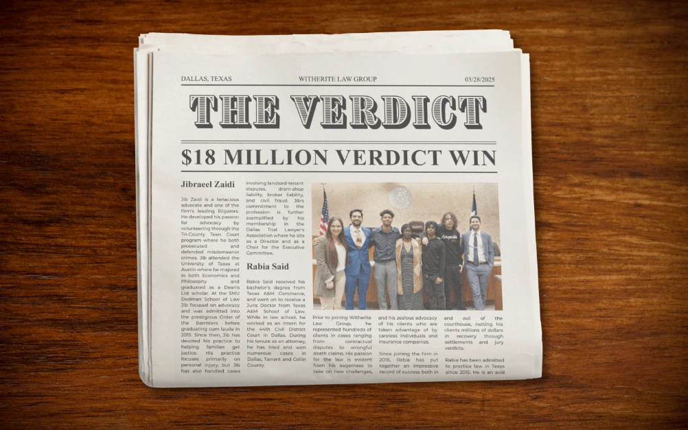 Newspaper clipping on a wooden desk with the headline "THE VERDICT $18 MILLION VERDICT WIN" featuring a photo of the winning legal team.
