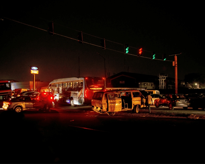 Busy intersection at night showing a traffic jam with several vehicles, including a bus and a van, stopped under a traffic light displaying green.