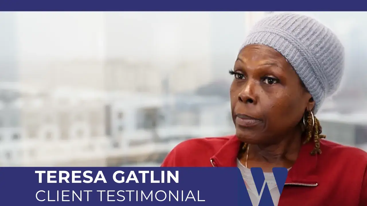 Video screenshot of Teresa Gatlin giving her client testimonial. She is wearing a red jacket and a light grey knit cap, with her name.