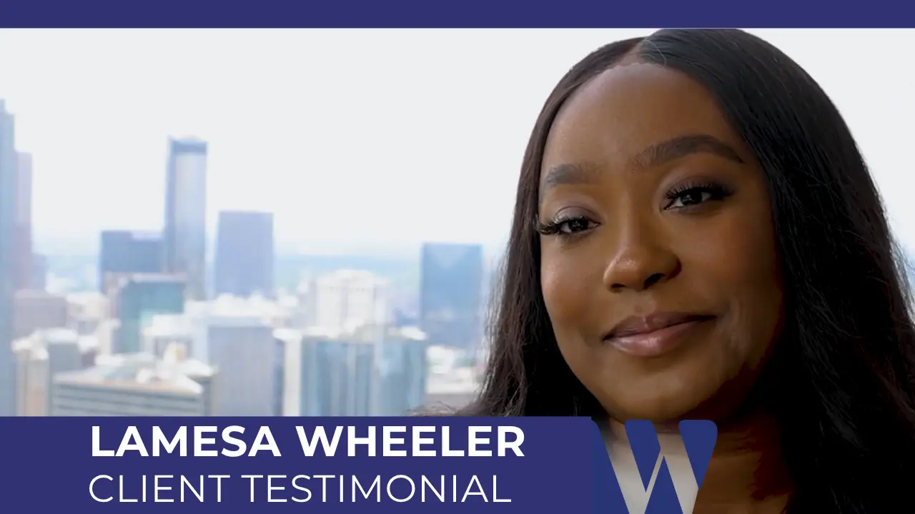 Lamesa Wheeler in a video interview setting, positioned in front of a modern city skyline background. She is a Black woman with dark hair and is wearing a gold-colored necklace and a dark top.