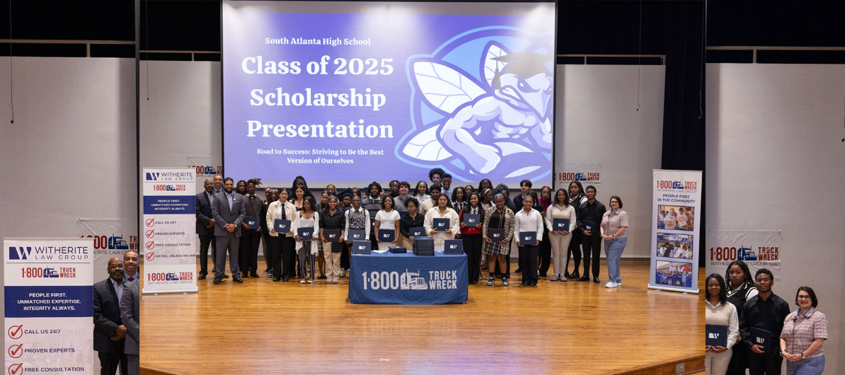Group photo on stage of the South Atlanta High School Class of 2025 Scholarship Presentation, with students holding certificates in front of a screen displaying the event title, flanked by sponsor banners.