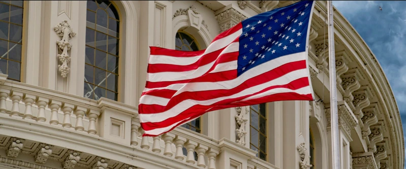 Close-up of the American flag waving proudly against the detailed architecture and marble façade of the US Capitol Building.